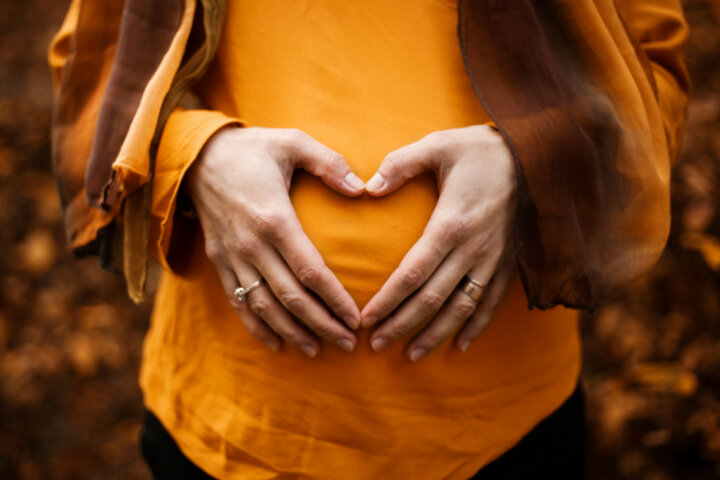 A pregnant woman in an orange shirt touching their belly.