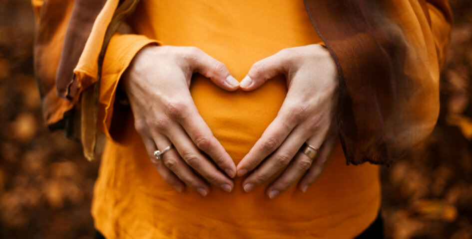 A pregnant woman in an orange shirt touching their belly.