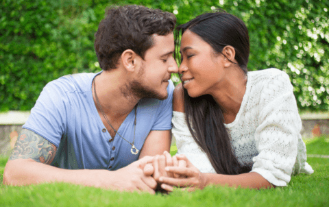 A couple leaning into each other on the grass.